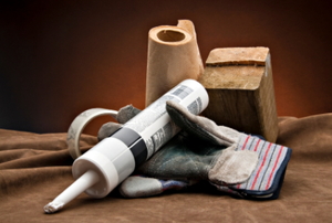 A roll of brown paper towels, some tape, a piece of wood, work gloves, and a tube of silicone caulking.