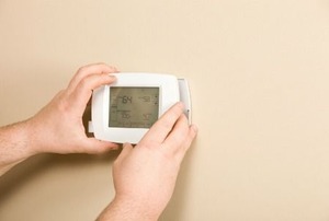 A person adjusting a programmable thermostat on the wall.