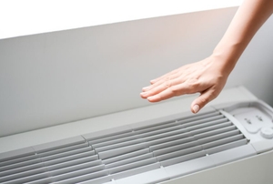 Someone using their hand to test the temperature of the air from an AC unit.