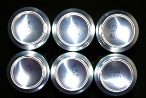 Six shining soda can bottoms against a black background.