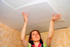 A woman installing a ceiling tile.