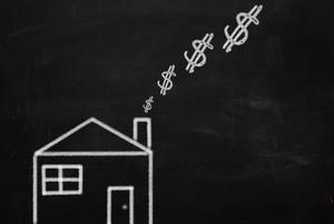 A house on a blackboard, with dollar signs emanating from its chimney.