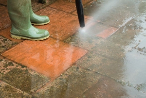 A pressure washer cleaning mildew off of a brick patio.