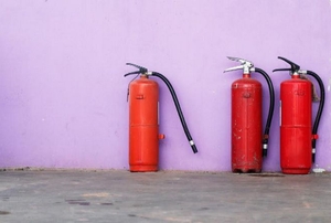 A trio of red fire extinguishers against a purple wall.