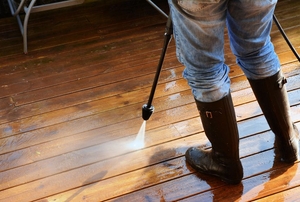A woman pressure washing a deck.