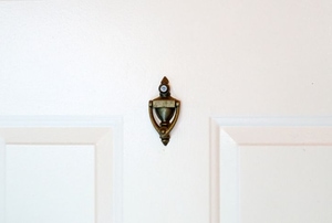 A white door with a door knocker and peephole on it. 