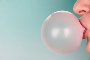 A person blowing a bubble with bubblegum against a blue background.