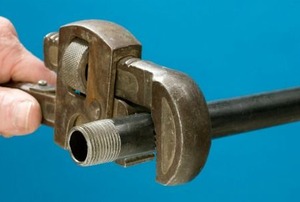 The threaded end of a black iron pipe and a pipe wrench.