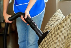 A person cleaning a sofa with a vacuum cleaner.