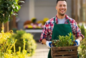 smiling man holding plants in a box at a garden center