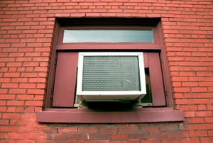 A window air conditioning unit installed in the window of a brick building.