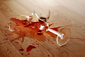 A broken wine glass on a hardwood floor with wine spilled everywhere.