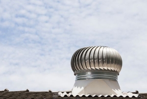 A turbine vent on a roof against a blue, cloudy sky.