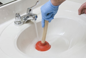 A man uses a plunger in a sink.
