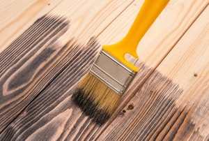applying brown stain to wood with paintbrush