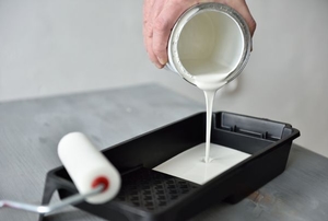 A quart of white paint being poured into a paint tray. 