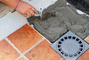 hand with cement trowel laying tile next to new drain