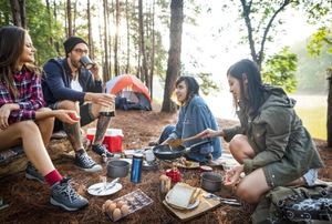 A group of friends gathering around a meal while camping.