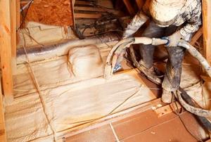 A worker pumping white foam insulation into an attic floor.