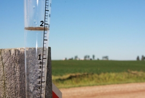 A simple rain gauge attached to a fence post on a rural farm.
