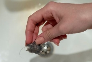 feminine hand pulling out hair from a tub drain