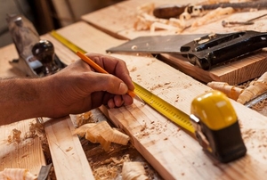 A woodworker measuring a piece of lumber on a work surface.