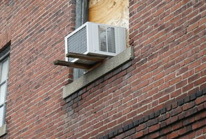 A window in a brick apartment with an air conditioner in it.