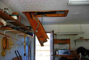 Side view of an open attic door, showing the attached ladder, not extended.