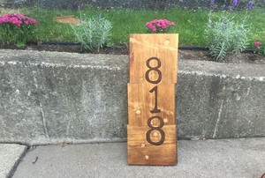 A house marker made of reclaimed wood leaning up against a concrete sidewalk.
