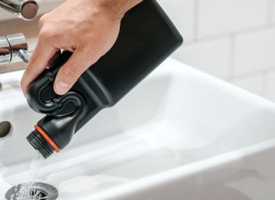 hand pouring chemicals into a sink drain