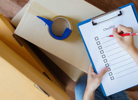 hands with checklist near moving boxes and tape