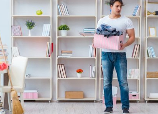 person moving box full of home goods in room with open shelving