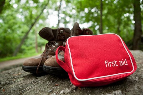 A pair of hiking boots and a first aid kit on a rock with trees in the background. 