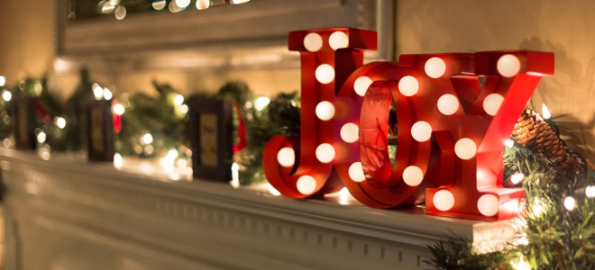 A red metal light-up sign that reads Joy on the edge of a mantel.