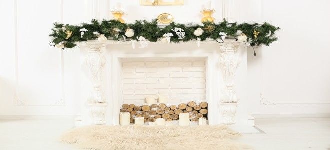 A white fireplace and mantel with Christmas decor including a garland and candles.