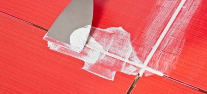 A putty knife scraping grout on red tile.