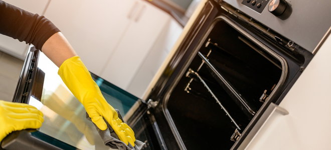 A woman with yellow gloves on cleaning an oven. 