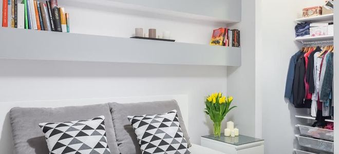 A bedroom with storage shelves above the bed.
