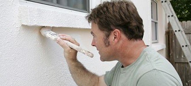 Painter at work applying white to the exterior of a home.
