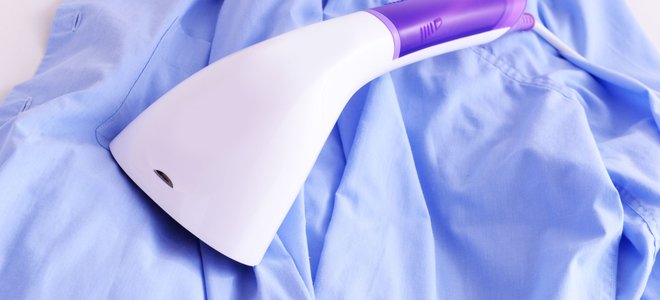 A purple-and-white handheld garment steamer lying on top of a blue shirt.