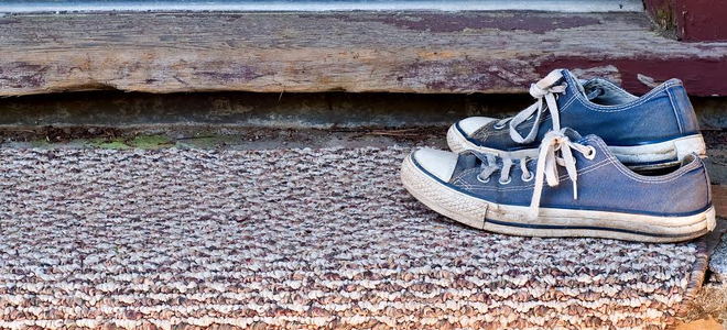 A pair of blue sneakers on a doormat outside a front door. 