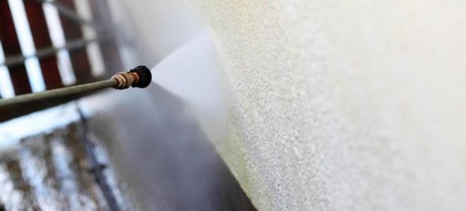 Spraying a stucco wall with a pressure washer.