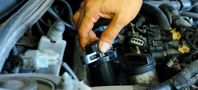 A hand securing an ignition coil in place inside an engine.