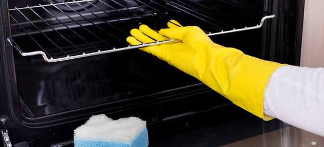 A gloved hand cleaning an oven with a sponge. 