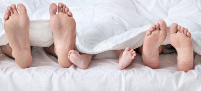 Three sets of feet peaking out from white bedding