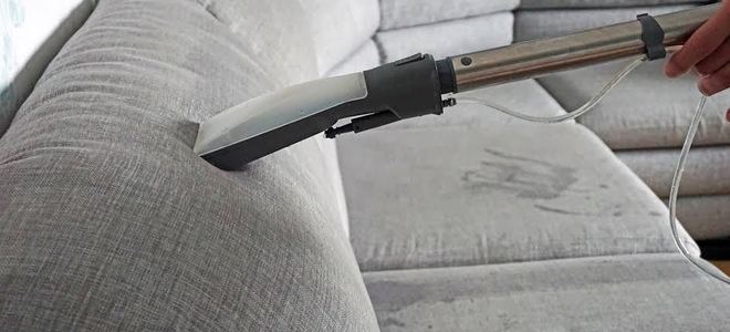 A vacuum cleaning a gray couch.