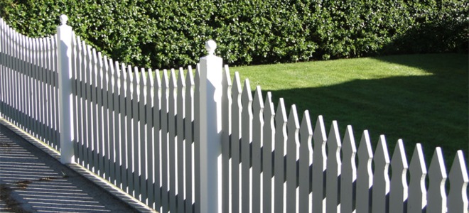 A white picket fence next to a large hedge.