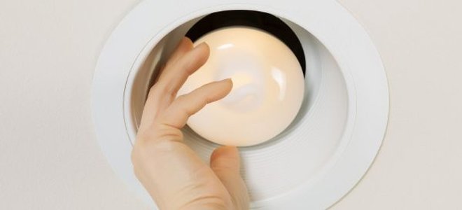 A recessed light with a hand adjusting the bulb.