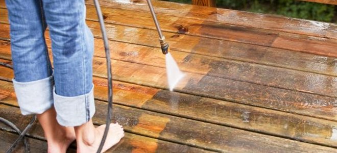 woman pressure washing a deck