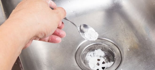 Someone putting baking soda into a stainless steel sink. 